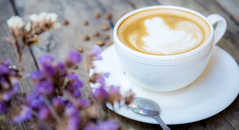 En latte i en kaffekopp på en träbänk med blommor i förgrunden. 