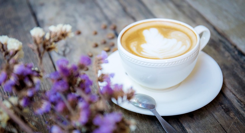 En cafe ó lait i en kaffekopp på en träbänk med blommor i förgrunden. 