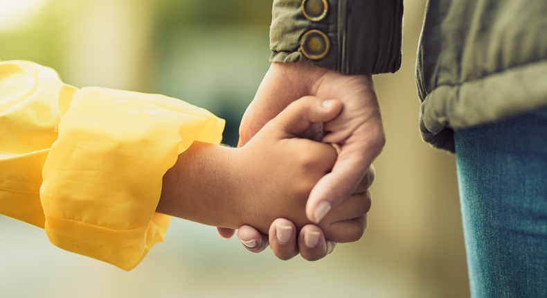 Ett barn i gul regnjacka håller en vuxen i handen. 